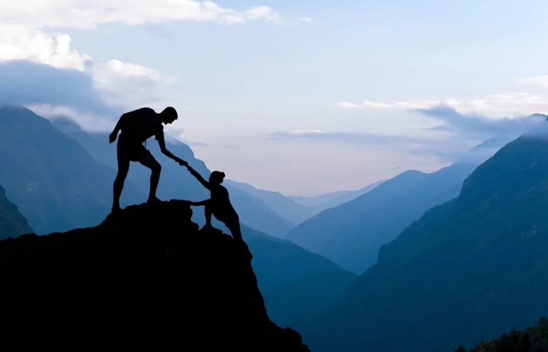 Mountain silhouettes: an outstretched hand helping someone reach the summit